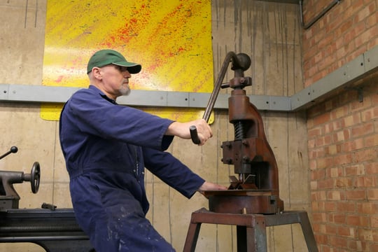 Oudere werknemer aan het werk met een handpers in een werkplaats